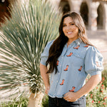 Women wearing a denim top with red boots embroidered on it outdoors. 