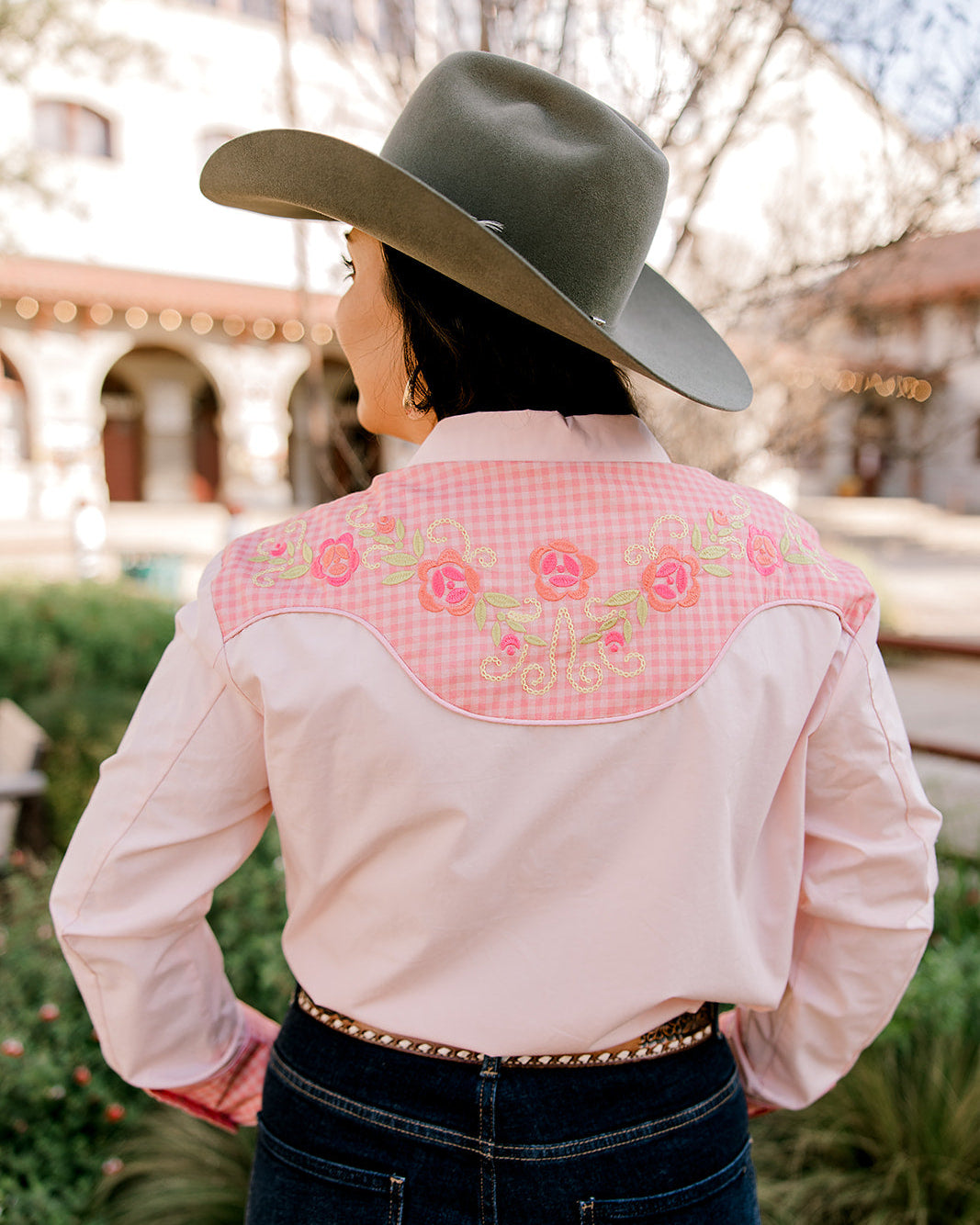 Person wearing a pink embroidered shirt with a wide-brimmed hat outdoors.
