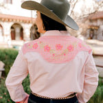 Person wearing a pink embroidered shirt with a wide-brimmed hat outdoors.