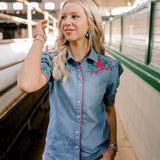 Women wearing a denim pearl snap top with pink western floral embroidery and green leaves. 