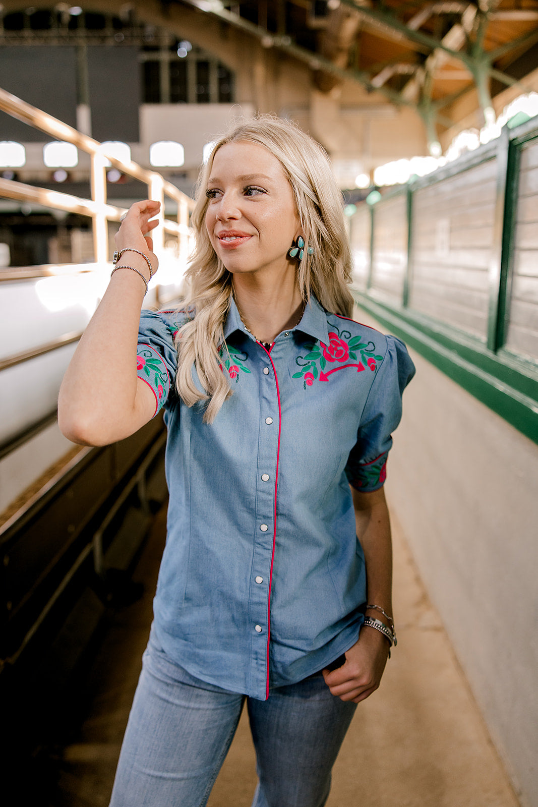 Women wearing a denim pearl snap top with pink western floral embroidery and green leaves. 