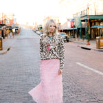 Woman in a leopard print top and pink skirt walking on a street with 'Fort Worth Stock Yards' sign in the background.