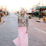 Woman in a leopard print top and pink skirt walking on a street with 'Fort Worth Stock Yards' sign in the background.