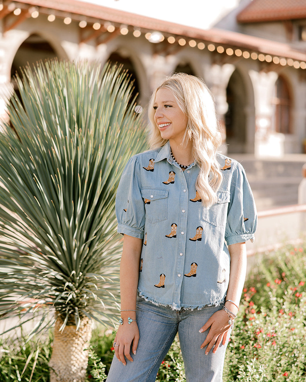 Women wearing a denim top with burnt orange boots embroidered on it outdoors. 