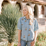 Women wearing a denim top with burnt orange boots embroidered on it outdoors. 