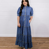 Woman wearing a blue denim dress standing on a wooden floor with a white wall background