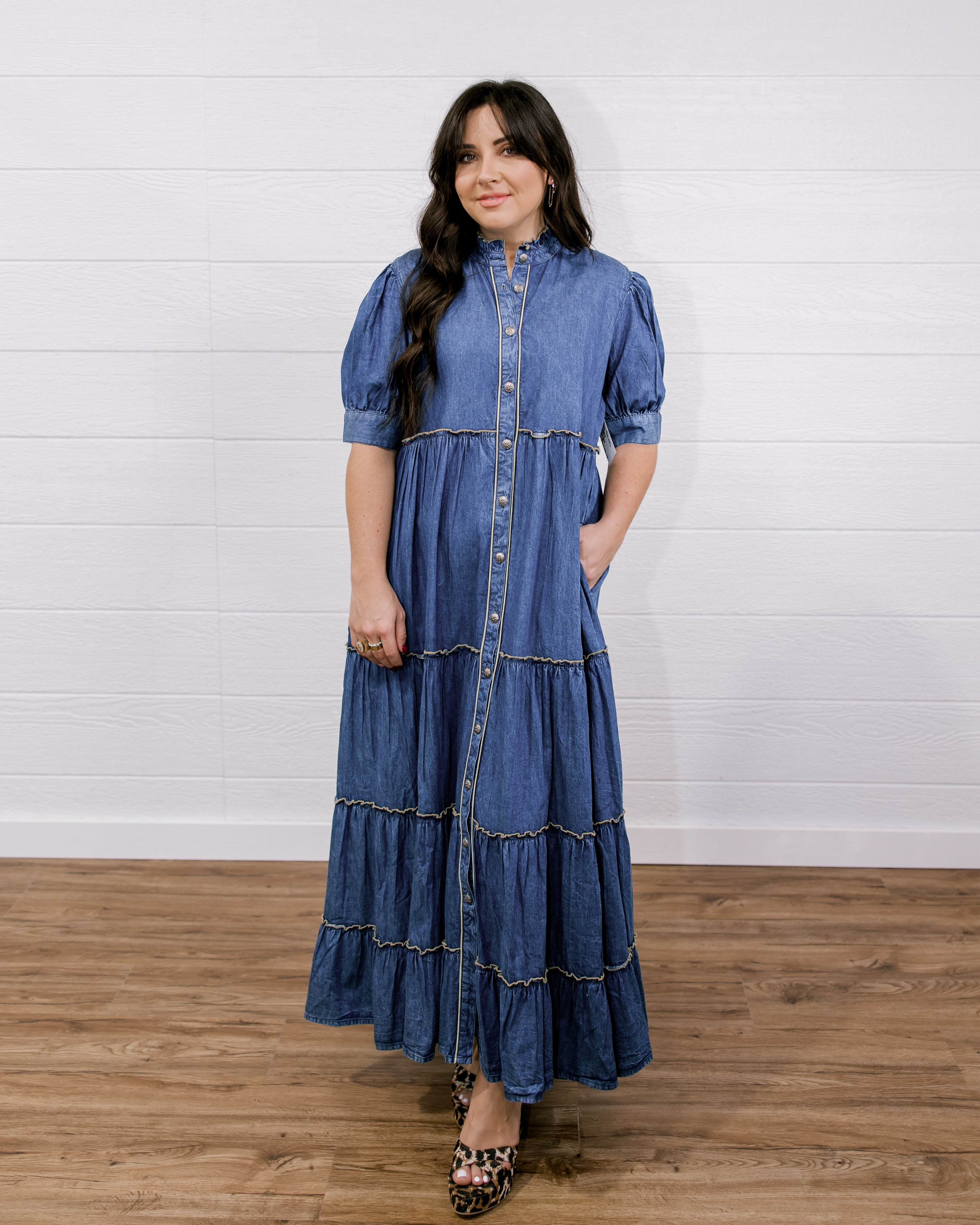 Woman wearing a blue denim dress standing on a wooden floor with a white wall background