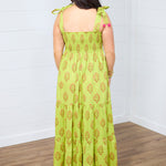 Woman with dark hair standing in a back profile position wearing the Addison Maxi Dress against a white background. The image focal point is of the back of the dress showing off the graphics and sleeveless top. 