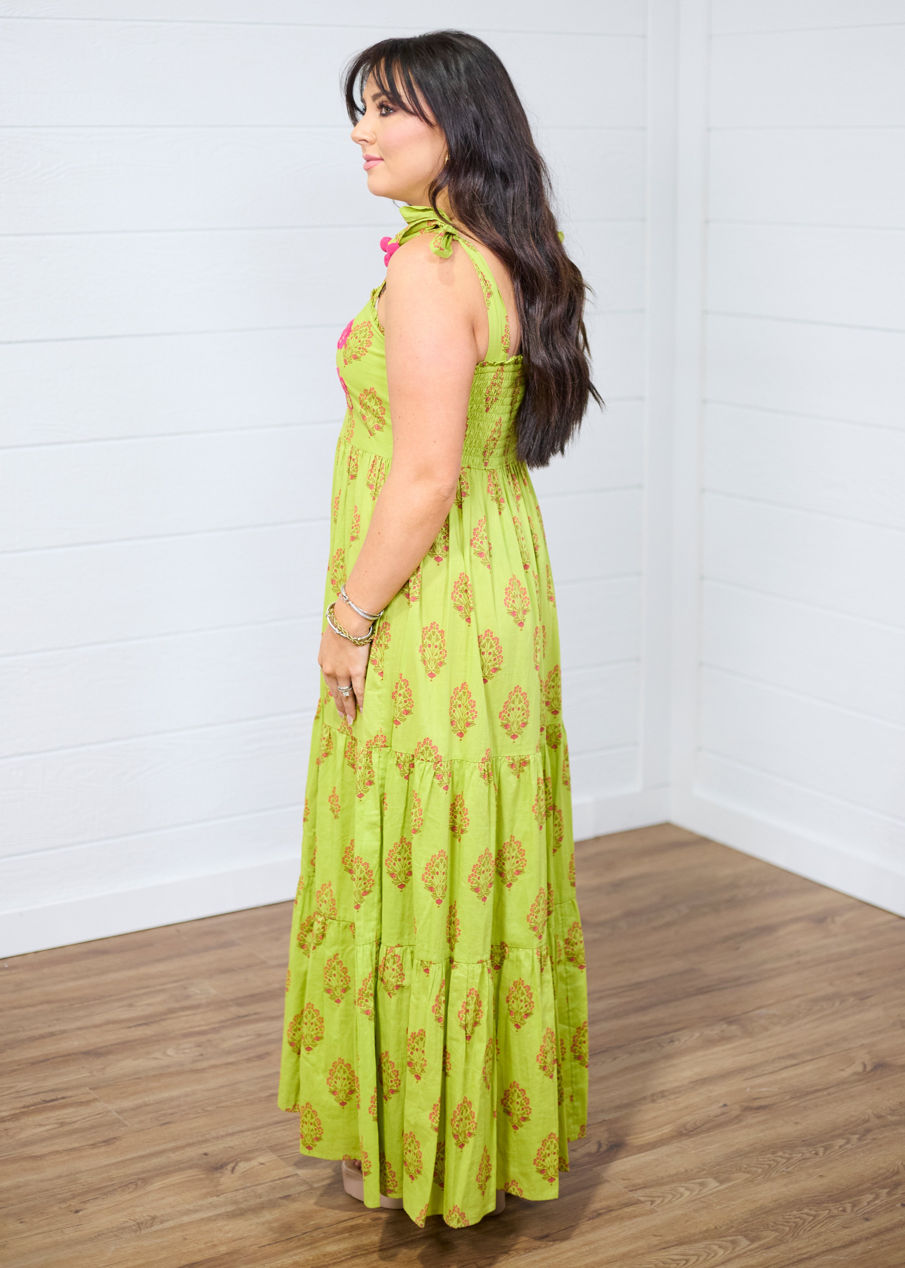 Woman with dark hair standing in a side profile position wearing the Addison Maxi Dress against a white background. The focal point of this image is the side of the dress, emphasizing the graphics and the sleeveless straps. 