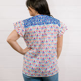 Women wearing a colorful top with blue ebroidery on the top showing the back on a white background 