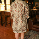 Woman with dark hair wearing a midi long-sleeve dress with cowboy graphics. Model paired this dress with brown and white booties. 