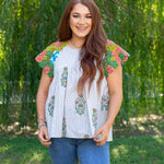 Woman with red hair standing in a front facing position in a lifestyle scene. The back ground shows a lot of greenery, and woman hair top paired medium-wash jeans.
