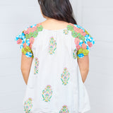 Woman with dark brown hair standing in back profile to show off back of the Asher Top. She is against a white background, and paired the top with light-wash denim jeans. 