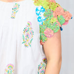 Woman with dark hair standing against a white background with a deep focal focus on sleeve of top. Top shows in depth pinwheel fabric on sleeve to give a better perception of detail. 