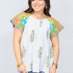 Woman with dark hair standing in a front facing position wearing the Asher Top. Focal point is on graphic details on front side of top. Woman has top paired with light-wash denim jeans. 