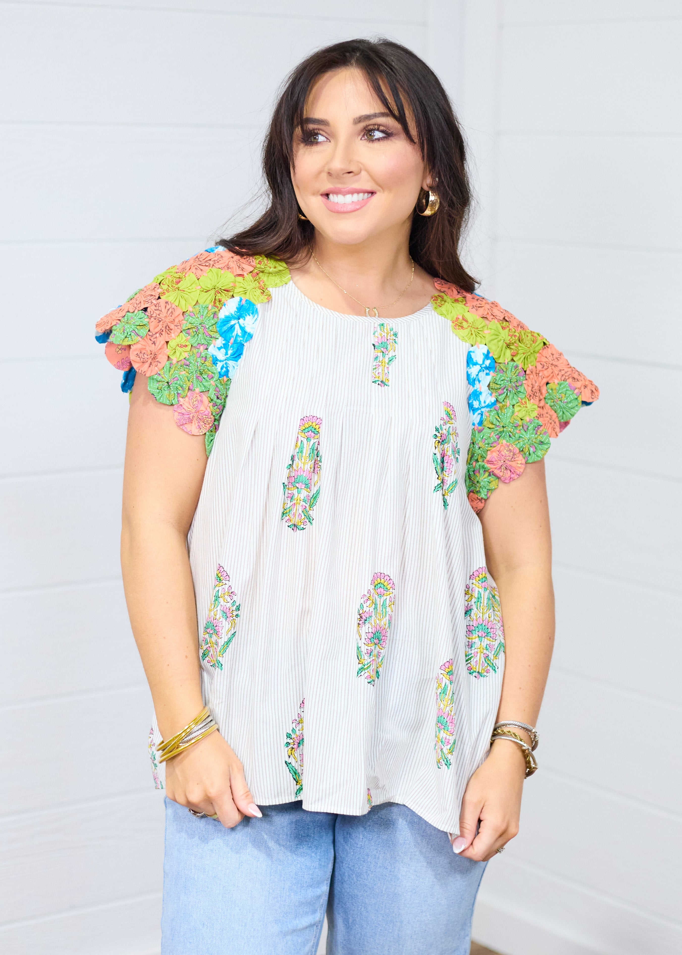 Woman with dark hair standing in a front facing position wearing the Asher Top. Focal point is on graphic details on front side of top. Woman has top paired with light-wash denim jeans. 