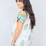 Woman with dark brown hair standing against a white back ground in a side profile position. Shows woman in a pair of light-wash denim jeans. 