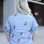 Woman with blonde hair standing in a back profile position wearing a short-sleeve denim top with red embroidered boots. The model paired this top with light-wash denim jeans. 