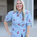 Woman with blonde hair wearing a short-sleeve denim top with red embroidered boots. The model paired this top with light-wash denim shorts. 