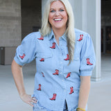 Woman with blonde hair wearing a short-sleeve denim top with red embroidered boots. The model paired this top with light-wash denim shorts. 