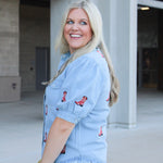 Woman with blonde hair wearing a short-sleeve denim shirts with red embroidered boots. The model paired this top with light-wash denim jeans. 