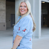 Woman with blonde hair wearing a short-sleeve denim shirts with red embroidered boots. The model paired this top with light-wash denim jeans. 