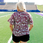 Woman with blonde hair wearing short sleeve top with floral graphics and black shorts. 