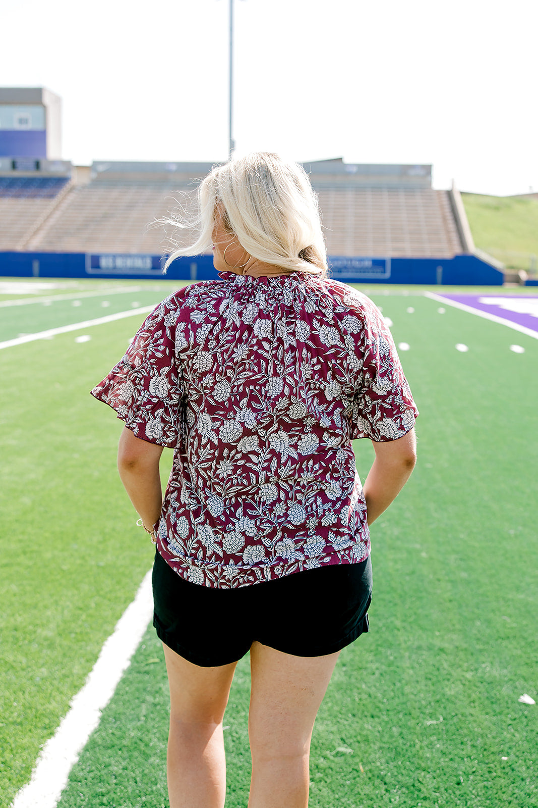 Woman with blonde hair wearing short sleeve top with floral graphics and black shorts. 