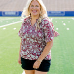 Woman with blonde hair wearing short sleeve top with floral graphics and black shorts. 