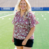 Woman with blonde hair wearing short sleeve top with floral graphics and black shorts. 