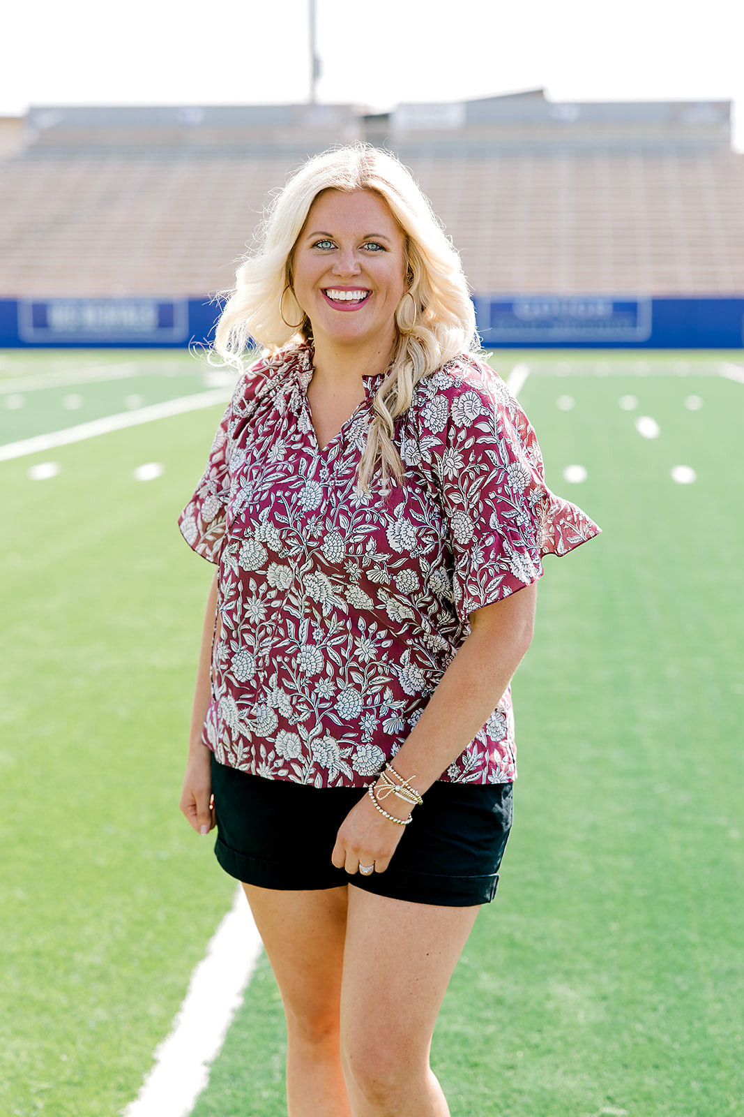 Woman with blonde hair wearing short sleeve top with floral graphics and black shorts. 