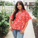 Woman with dark hair standing in a front profile position wearing the Bell Top in a lifestyle scene. The focal point of this image is the floral, tassels, and v-neckline. The model paired this top with light-wash denim jeans. 