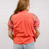 Person wearing a coral shirt with floral sleeves against a light background facing back. 