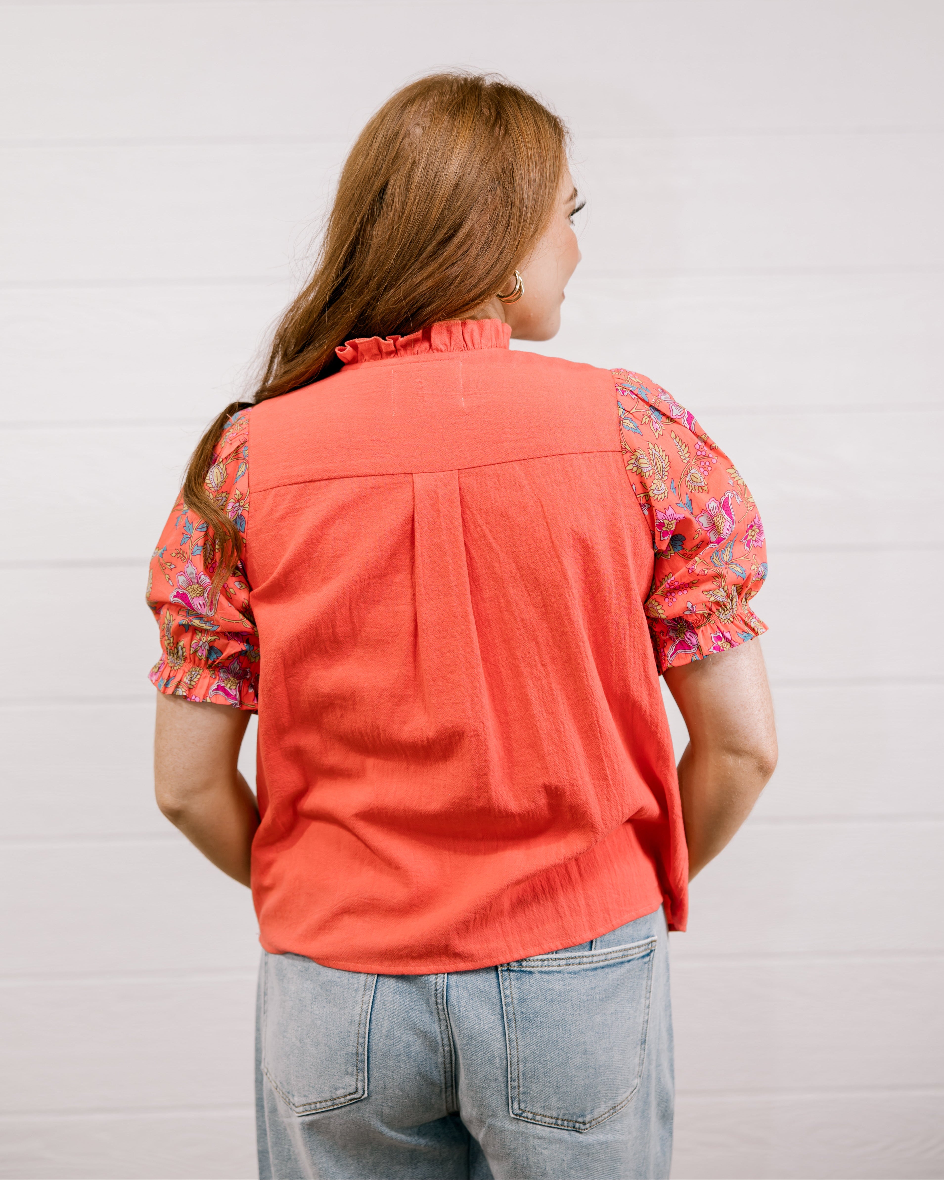 Person wearing a coral shirt with floral sleeves against a light background facing back. 