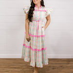 Woman wearing a checkered dress with pink accents against a white wall facing the front. 