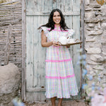Woman in a checkered dress standing in front of a rustic wooden door.