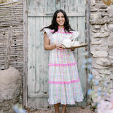 Woman in a checkered dress standing in front of a rustic wooden door.