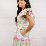 Woman wearing a colorful dress with pockets with a white background facing the side. 
