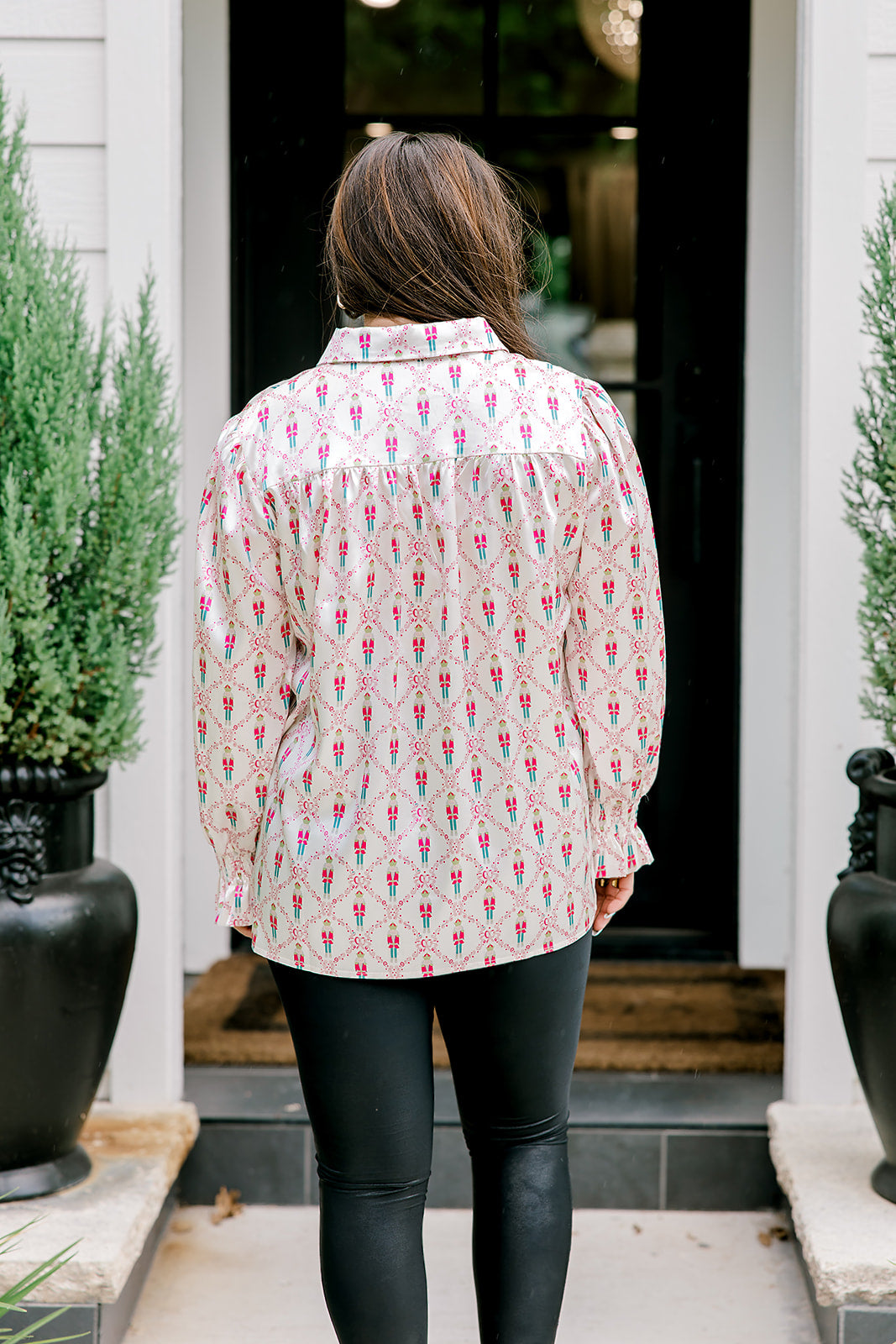 Woman with dark hair wearing a long-sleeve silky top with nutcracker graphics. Model paired this top with faux leather leggings. 
