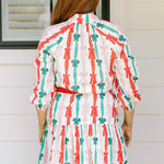 Woman with red hair wearing a long-sleeve dress with pink, red, and green graphic bows. Dress comes with red-fabric that is tied in front. 