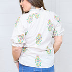 Woman with dark hair showing the Courtney Top in a back profile position against a white background. She paired the top with dark-wash denim shorts. 