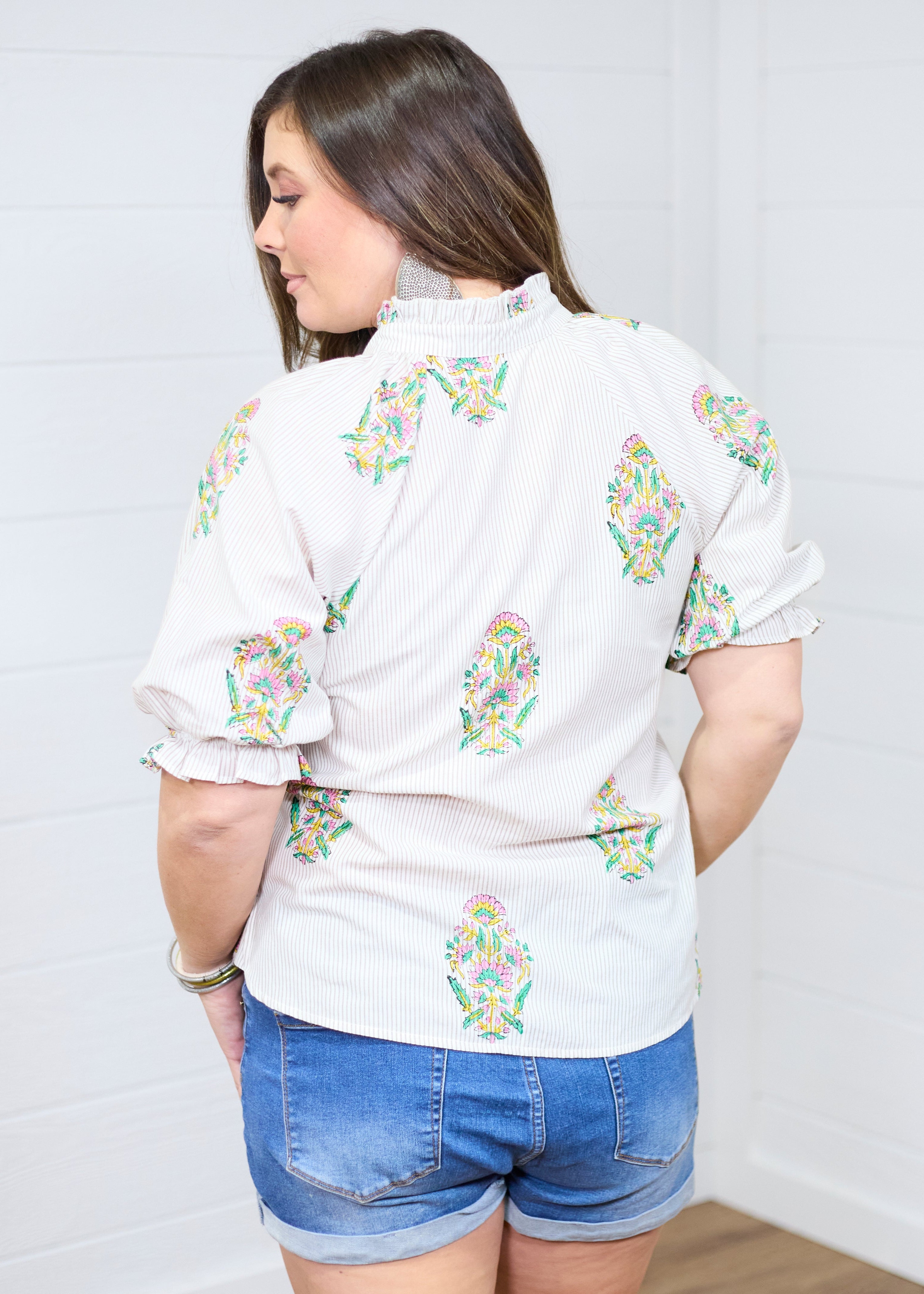Woman with dark hair showing the Courtney Top in a back profile position against a white background. She paired the top with dark-wash denim shorts. 