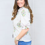Woman with dark hair in a side profile position with the Courtney Top against a white background. This image is showing the side profile and sleeves of top. She has the top paired with dark-wash denim shorts. 