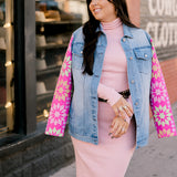 Woman wearing a pink dress with a patchwork denim jacket on a city street.