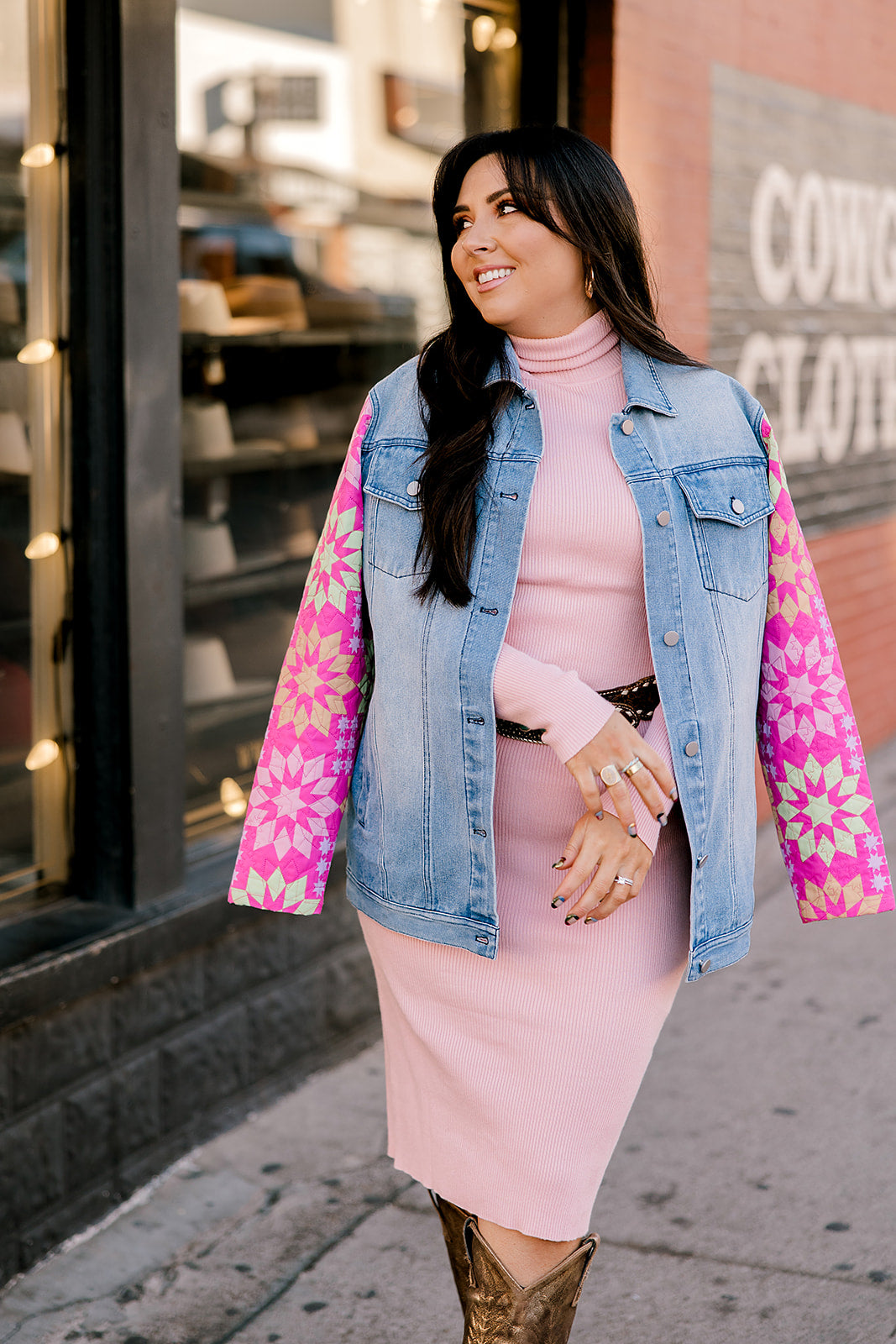 Woman wearing a pink dress with a patchwork denim jacket on a city street.