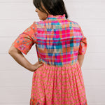 Woman wearing a colorful checkered dress against a white background facing the back. 