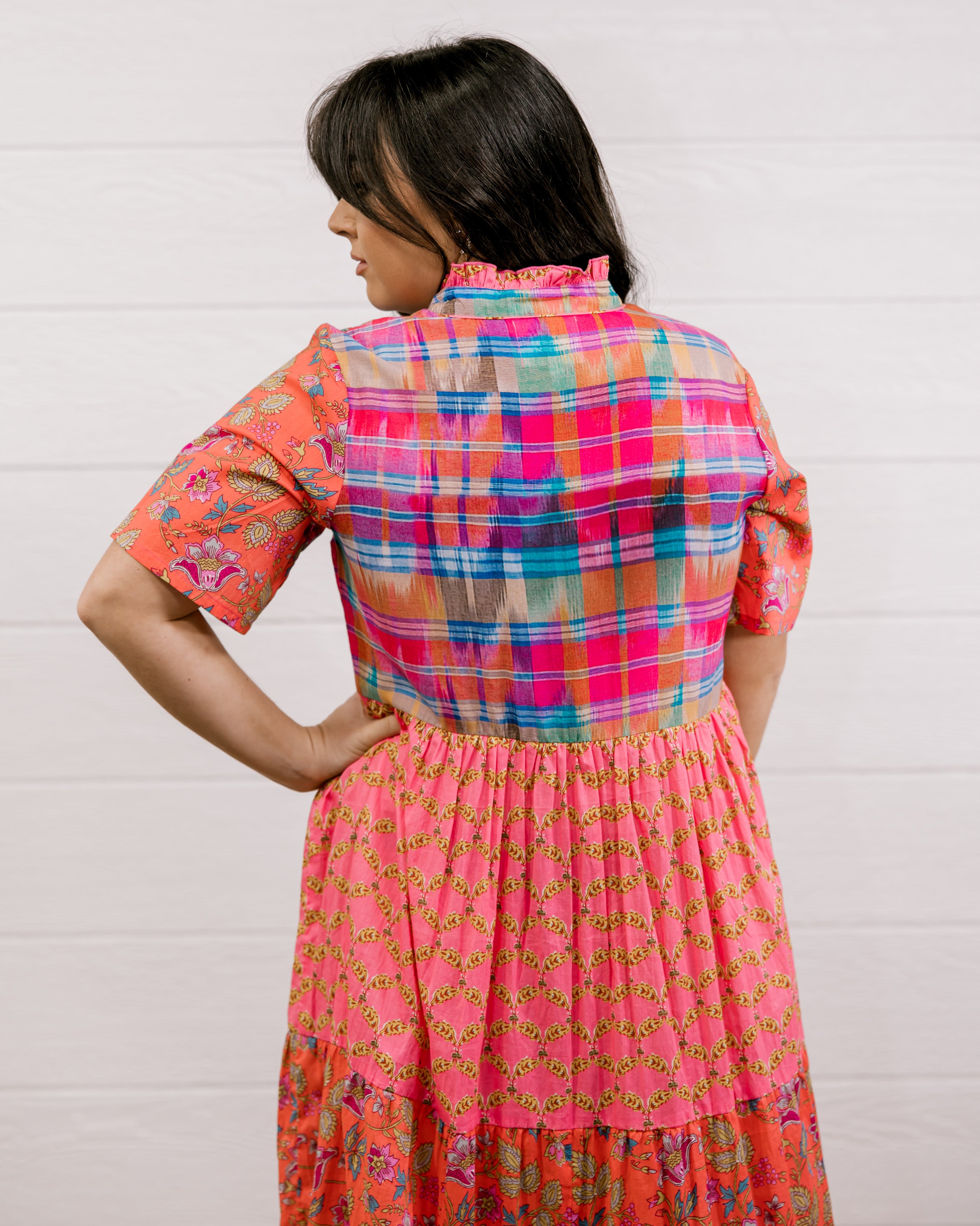 Woman wearing a colorful checkered dress against a white background facing the back. 