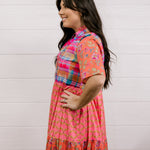 Woman wearing a colorful dress against a white wall facing the side. 