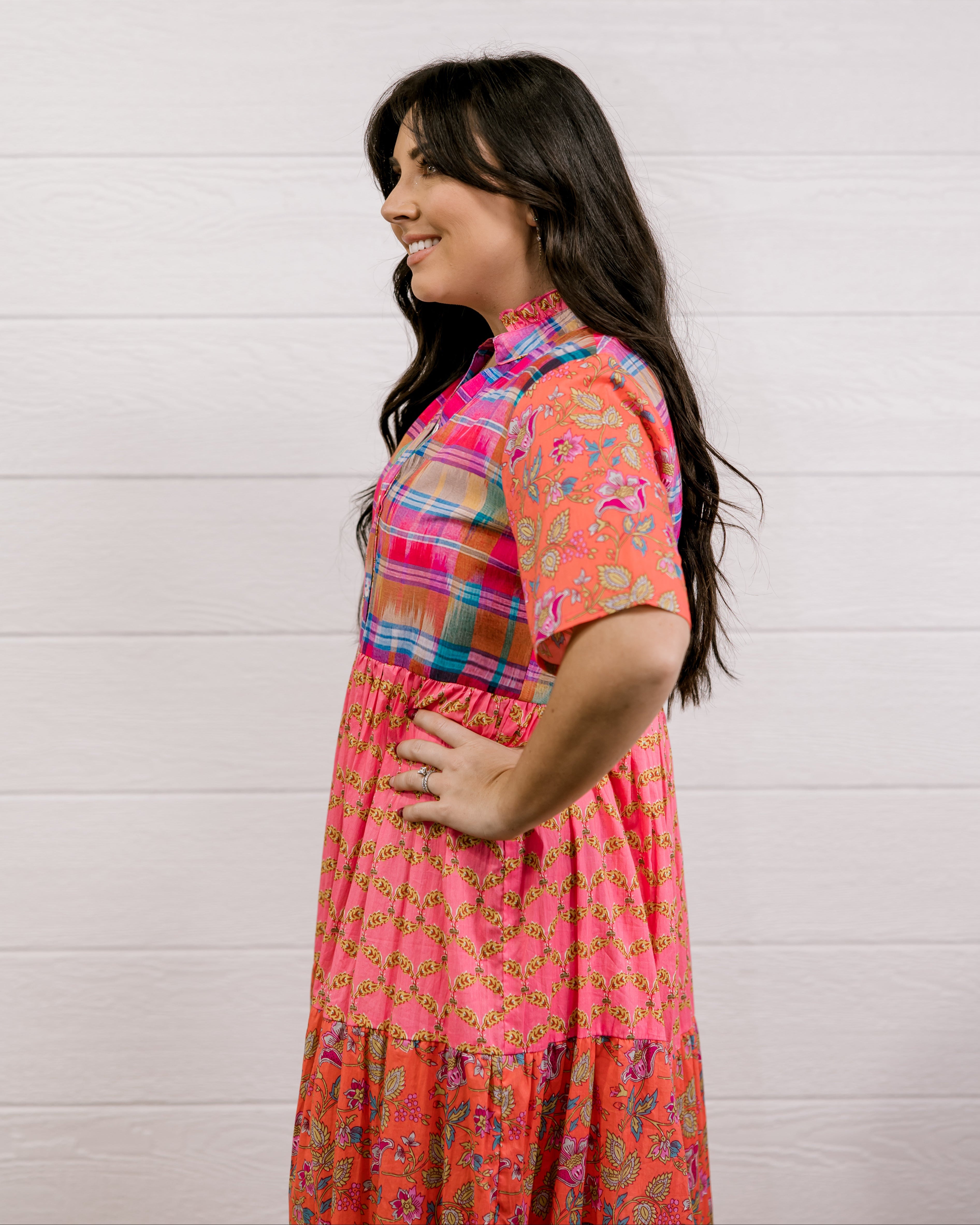 Woman wearing a colorful dress against a white wall facing the side. 
