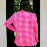 Woman with dark hair wearing a pink tweed blazer with gold buttons. Model paired blazer with dark-wash denim jeans. 